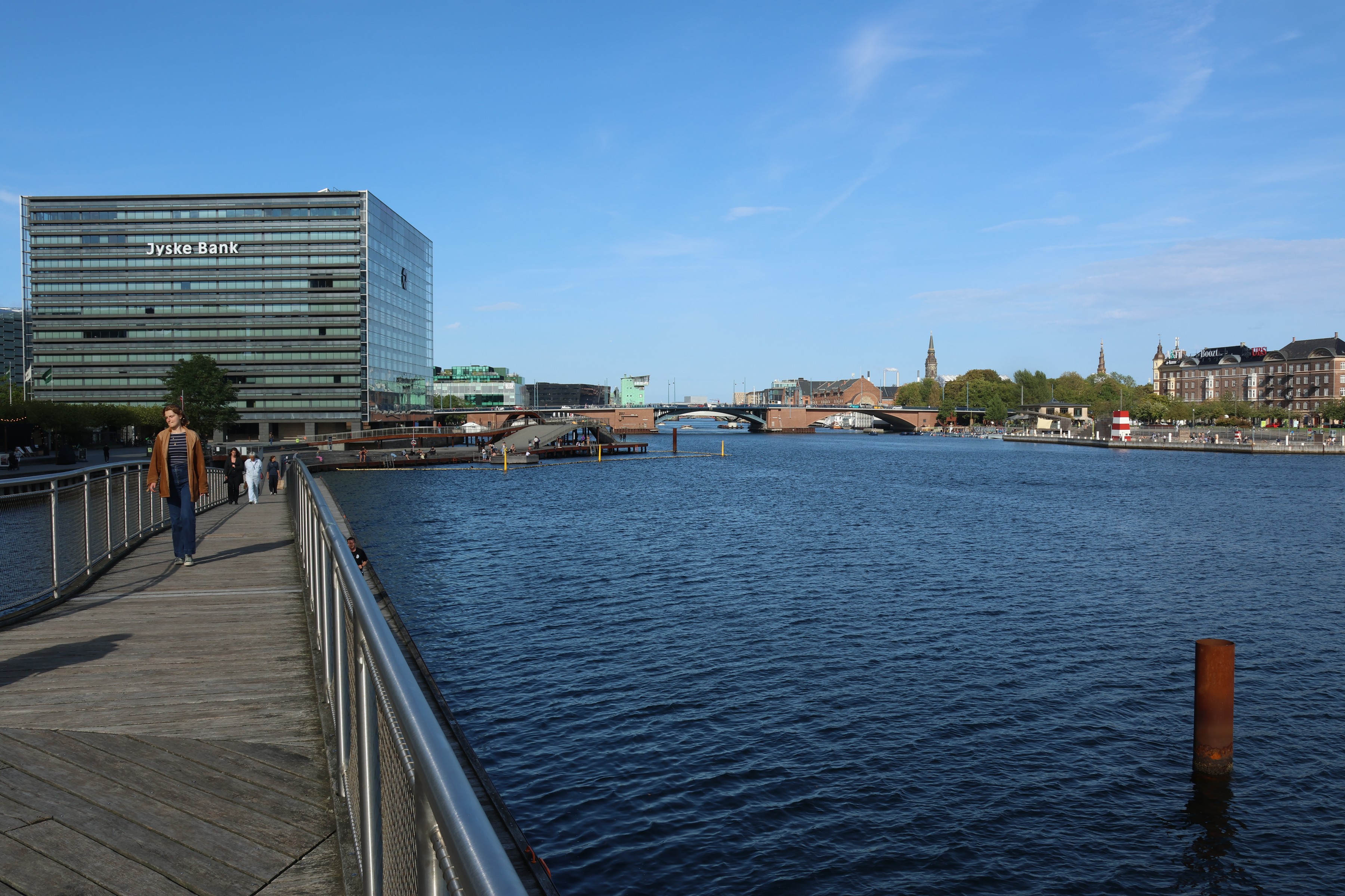 A wooden promenade running along the harbour past a glass office block