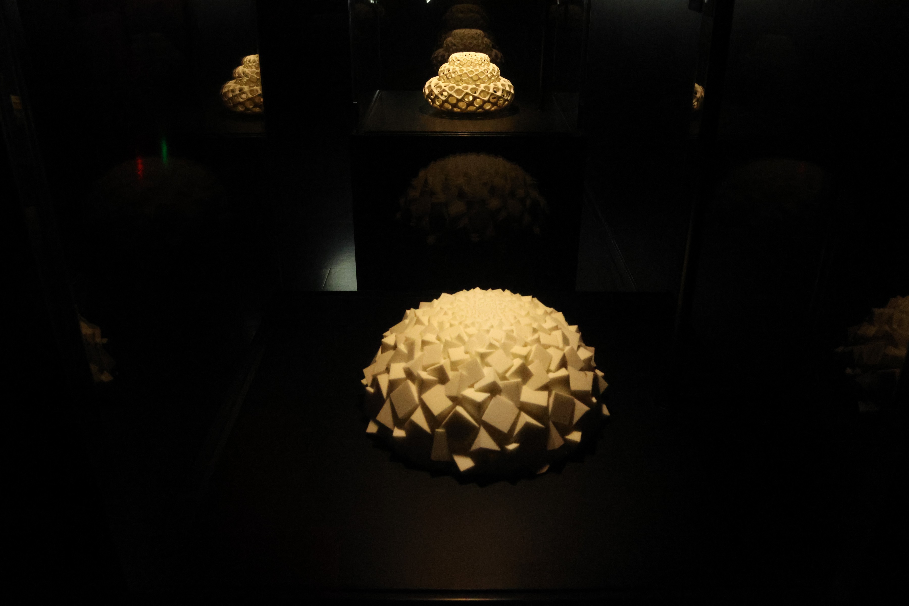 A faceted white sculpture lit in a mirrored vitrine