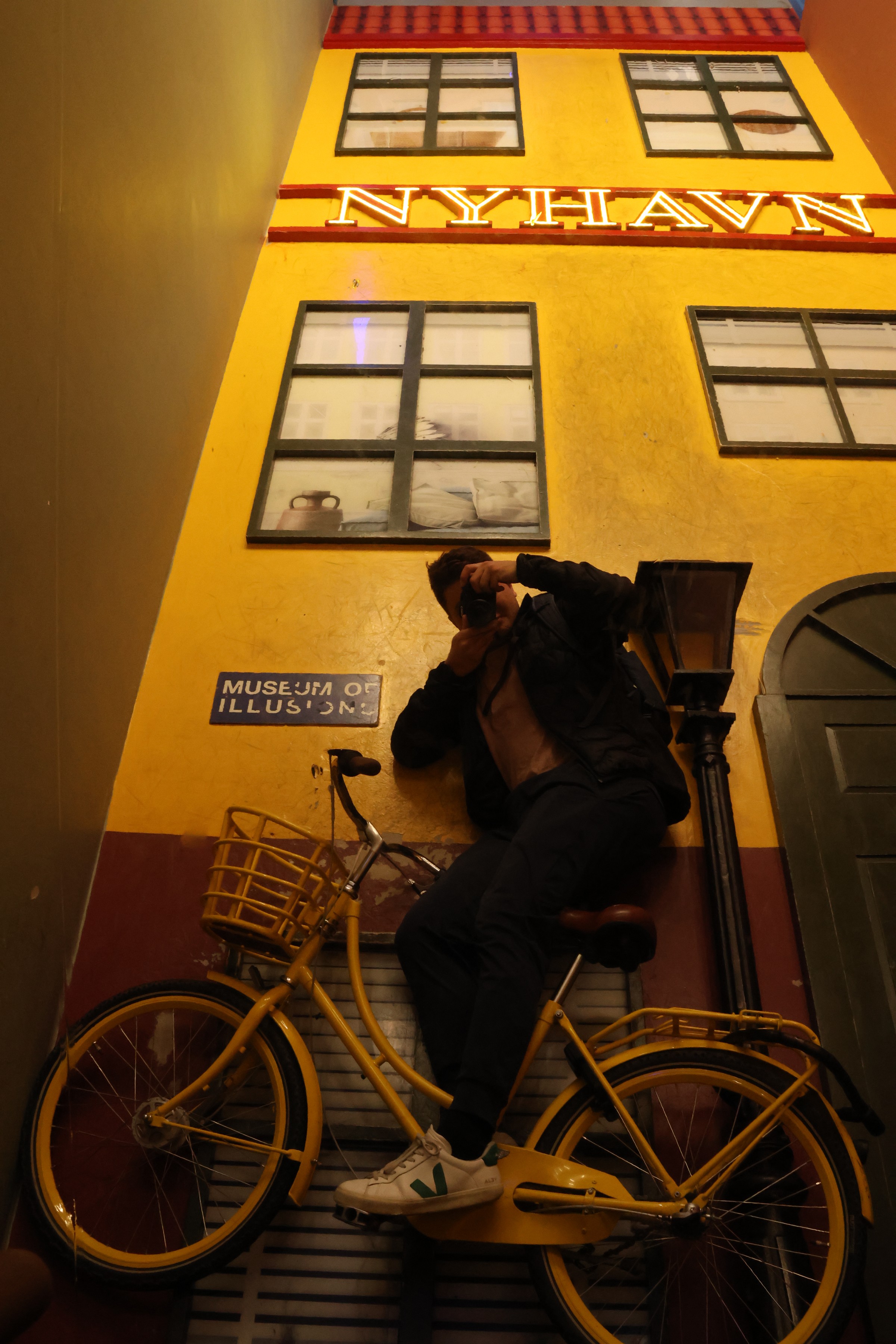 Leaning on a painted Nyhavn facade beside a yellow bicycle, with the floor standing in for a wall