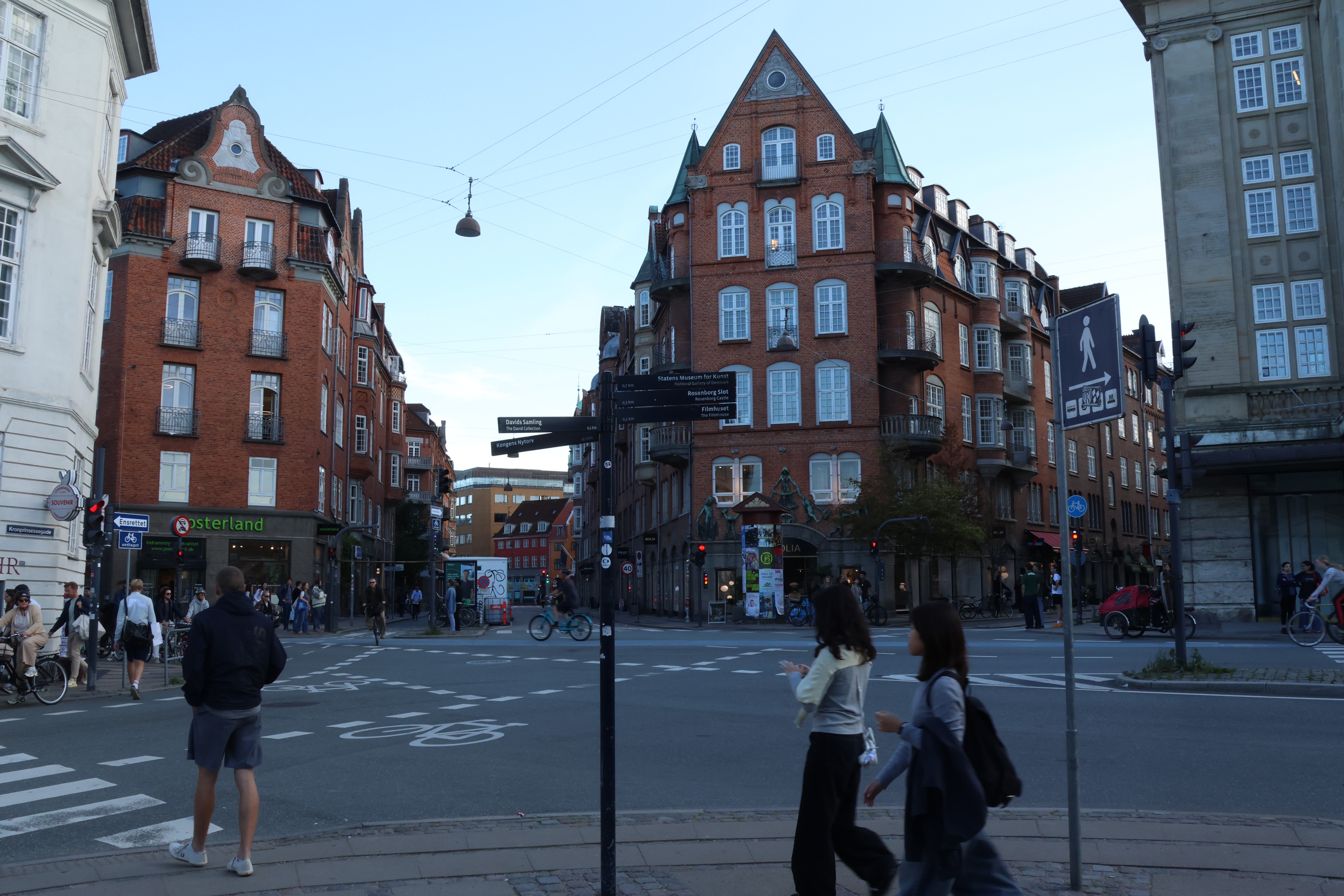 Pedestrians crossing a junction below red-brick gables in the evening light