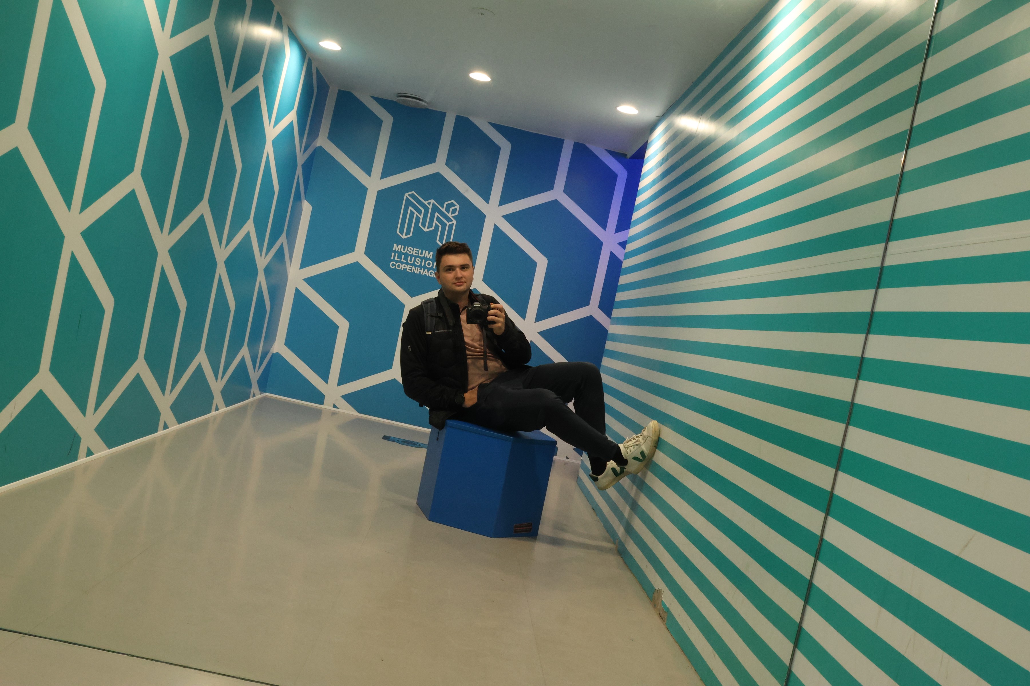 Sitting on a blue cube in a tilted room, apparently holding a pose against gravity
